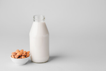 Bottle of tasty almond milk and bowl with nuts on light background