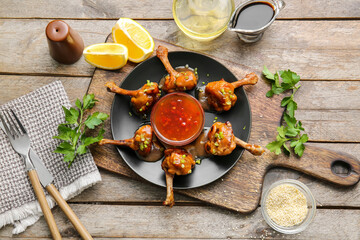 Plate with tasty chicken lollipops and sauce on wooden background