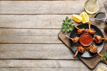 Fototapeta na wymiar Plate with tasty chicken lollipops and sauce on wooden background