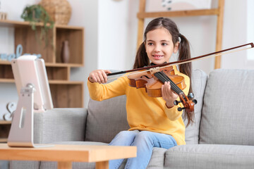 Little girl taking music lessons online at home