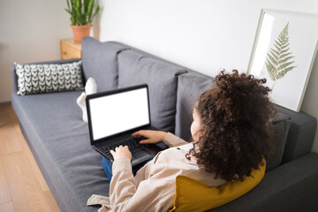 curly hair girl is lying on couch and looking at at computer screen laptop. blank white screen....