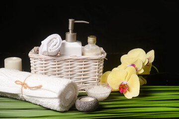 Beautiful spa setting bath spa in basket of orchid and rolled towel 
on pile of long bamboo stem background

