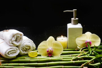 Beautiful spa setting of orchid and rolled towel ,candle, oil bottle 
on pile of long bamboo stem background



