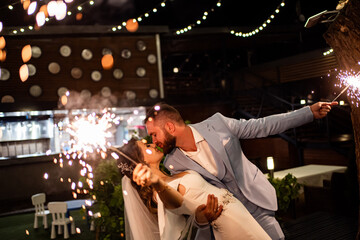 newlyweds with sparklers in night park with garlands in trees. ending to wedding