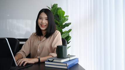 Cheerful businesswoman sitting at her workplace with computer laptop and smiling to camera.