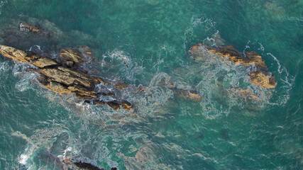 Aerial view of waves swirling around rocks in the ocean