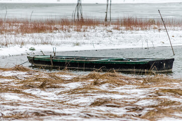 Fototapeta premium Forgotten wooden fishing boats in the frozen water of the Danube tributary, covered with snow. Vojvodina, Novi Sad, Serbia. 