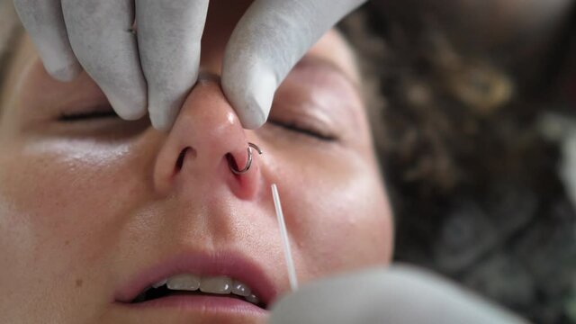 Professional piercer in the disposable gloves putting a ring into the nostril 