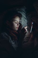 woman with a phone in her hands at night lying in bed rest before bedtime