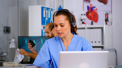 Specialist doctor nurse with headphones checking appointment during telehealth communication in...