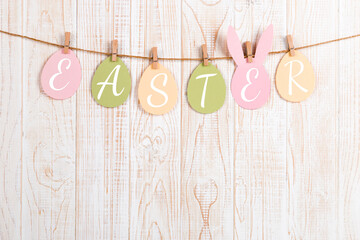 Inscription Easter on colored eggs, on a wooden background, a rope with clothespins. The concept of postcards for the Easter holiday.