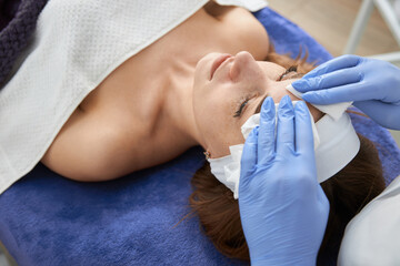 Professional cosmetologist is doing procedures for client in light cabinet