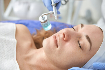 Professional cosmetologist is doing procedures for client in light cabinet