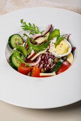 Close-up tasty vegetable salad with egg, mozzarella and olive oil. Healthy food. Organic vegetables: Peking cabbage, cucumber, red onions, tomatoes, and arugula. Mediterranean diet. Vertical shot