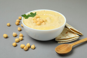 Bowl of hummus, pita and spoon on gray background