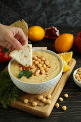 Female hand dips pita in tasty hummus on wooden table