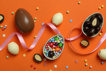 Obraz na płótnie Canvas Easter chocolate eggs, candies and sprinkles on orange background