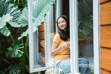 beautiful asian woman drinking coffee in the morning by the window. view from outside.