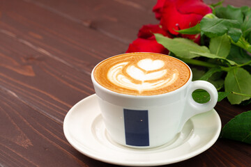 Cup of cappucino with art and bouquet of roses on wooden table