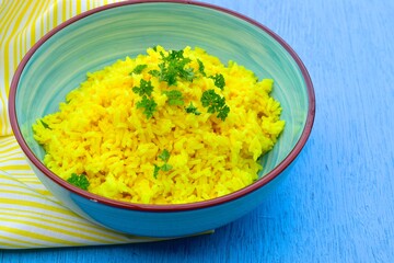 Indonesian yellow turmeric rice or Nasi Kuning in a bowl garnish with chopped parsley. Blue background