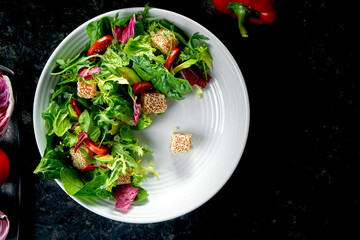 Mix salad with salmon, cherry tomatoes and avocado, served in a white plate on a dark marble background. Restaurant food.