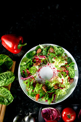 Warm salad mix with chicken liver and pomegranate served in a white plate on a dark marble background. Restaurant food.