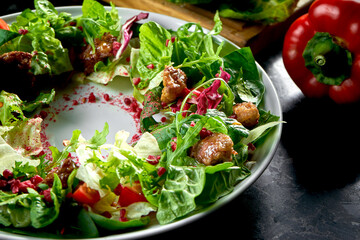 Warm salad mix with chicken liver and pomegranate served in a white plate on a dark marble background. Restaurant food.