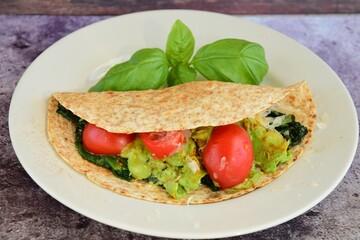 Whole wheat tortilla wrap filled with avocado, spinach and tomato garnish with basil leaf
