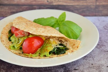 Whole wheat tortilla wrap filled with avocado, spinach and tomato garnish with basil leaf
