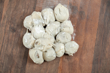 A wooden round board with uncooked dumplings and flour