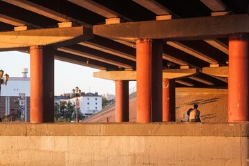 Obraz premium A couple in love is sitting under a car bridge between huge columns, in the light of the setting sun on a summer evening