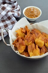 Deep fried beef wontons in a wok served with peanut sauce 

