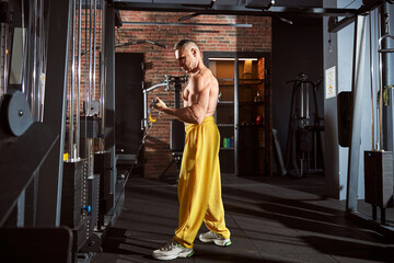 Muscled man in comfortable sportsgear working out at gym