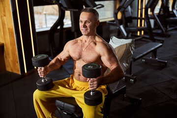Naklejka premium Gladsome gentleman with bare torso exercising at the gym