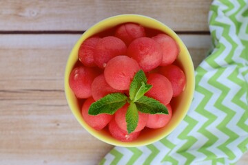 Watermelon balls in a bowl, garnish with mint leaf. Flat lay
