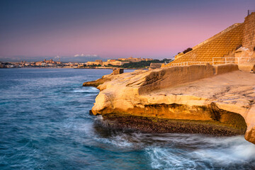 Rocky coastline of Malta and beautiful architecture of the Valletta city at dawn