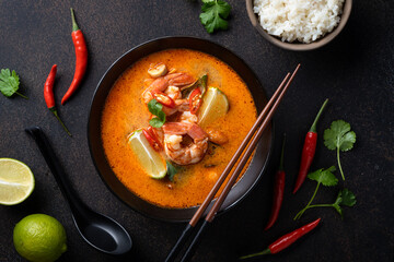 Tom Yum kung Spicy Thai soup with shrimp in a black bowl on a dark background, top view