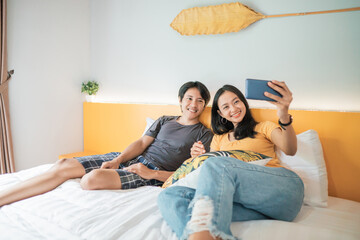 Beautiful young couple using smart phone and smiling while spending time in bed at home