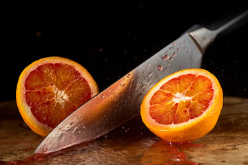 Blood orange cut with a knife juice splashes around.