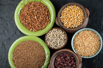 Different kinds of bean seeds, lentil, peas in dishes on a dark background