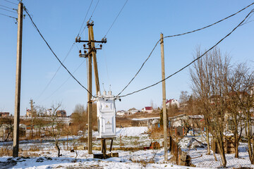 Electric transformer box on a village background. Electricity supply to the settlement. Power distribution equipment. Attention, high voltage zone. Outdoor concrete pillar electricity line. Landscape