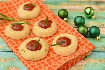 Homemade rosemary thumbprint cookies with jam on green wooden background. Decorated with Christmas green balls
