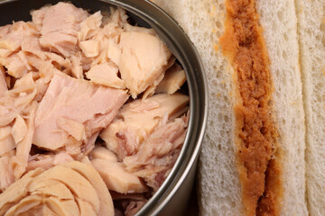 Tuna fish spread sandwich white bread on wooden board over tuna flake chunk in tin can black slate background
