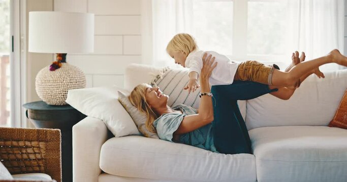 Mother and cute young kid playing on the couch laughing, family lifestyle at home