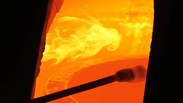 Traditional glass blower manufacturing process, working on a bubble of melted glass on a rod by heating it up by hand in a kiln at glass makers workshop.
