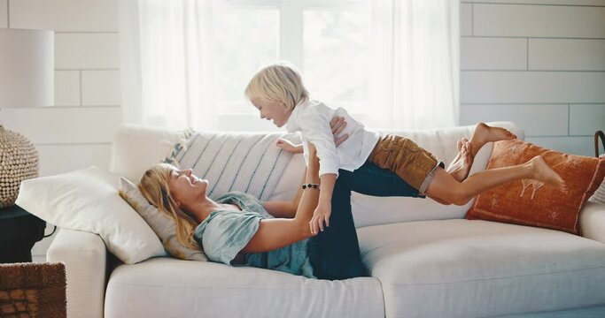 Mother and cute young kid playing on the couch laughing, family lifestyle at home