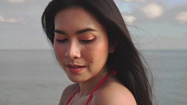 Portrait of young Asian beautiful woman in bikini smiling at camera. hair blowing in wind on tropical beach in summer weather. travel and lifestyle concept