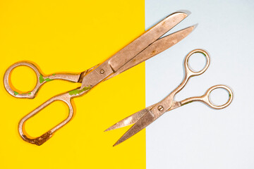 Closeup of Pair of Old Rusty Tailor Scissors Placed Over Blue And Yellow Paper Background.
