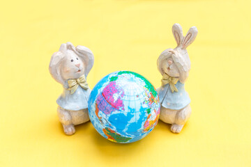 Two wooden rabbit doll with global ball on yellow background, Easter concept background