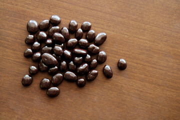 dark bitter chocolate candies, chocolate coverd raisin on wooden background, top view of sweets